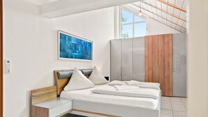 A modern bedroom with a bed, a bedside table, a wardrobe, a painting, and a window.