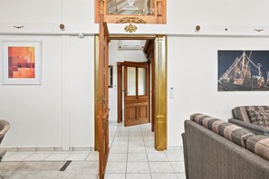 Ein Zimmer mit Holztür, einer Couch, einem gerahmten Bild und Fliesenboden.