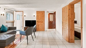 A spacious living area with a sofa, chairs, a TV, and wooden doors.