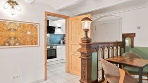 A dining area with a wooden table and chairs, a decorative lamp, and a kitchen visible through an open door.