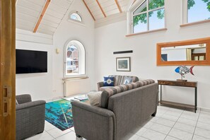 Ein Wohnzimmer mit einer Couch, Sesseln, einem Couchtisch, einem Fernseher, einem Kamin und einem großen Fenster.