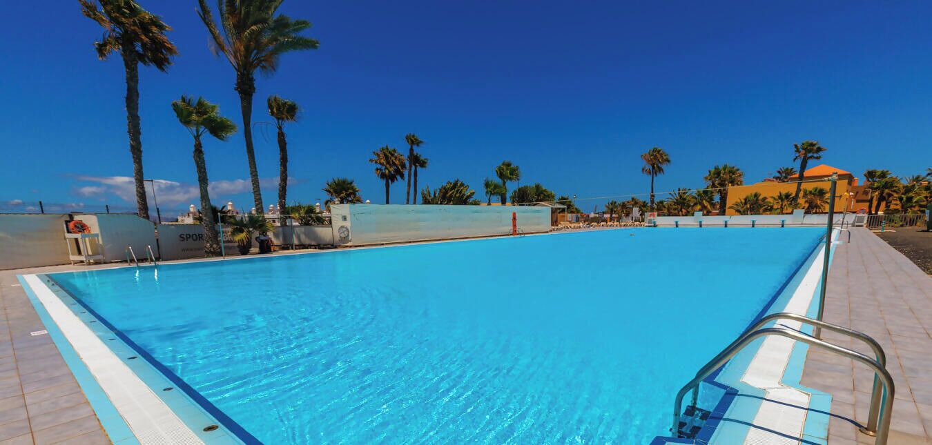 A clear blue swimming pool with a metal ladder and a tiled deck surrounding it.