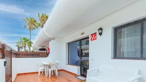 A balcony with white chairs, a small table, and a view of palm trees. - Dunasamor near to the Dunes by iRent Fuerteventura (Corralejo)