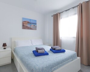 A hotel room with a bed, a nightstand, a lamp, and a window with curtains.