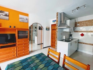 Une cuisine compacte avec un coin repas, des meubles en bois, un téléviseur et une nappe à motifs.