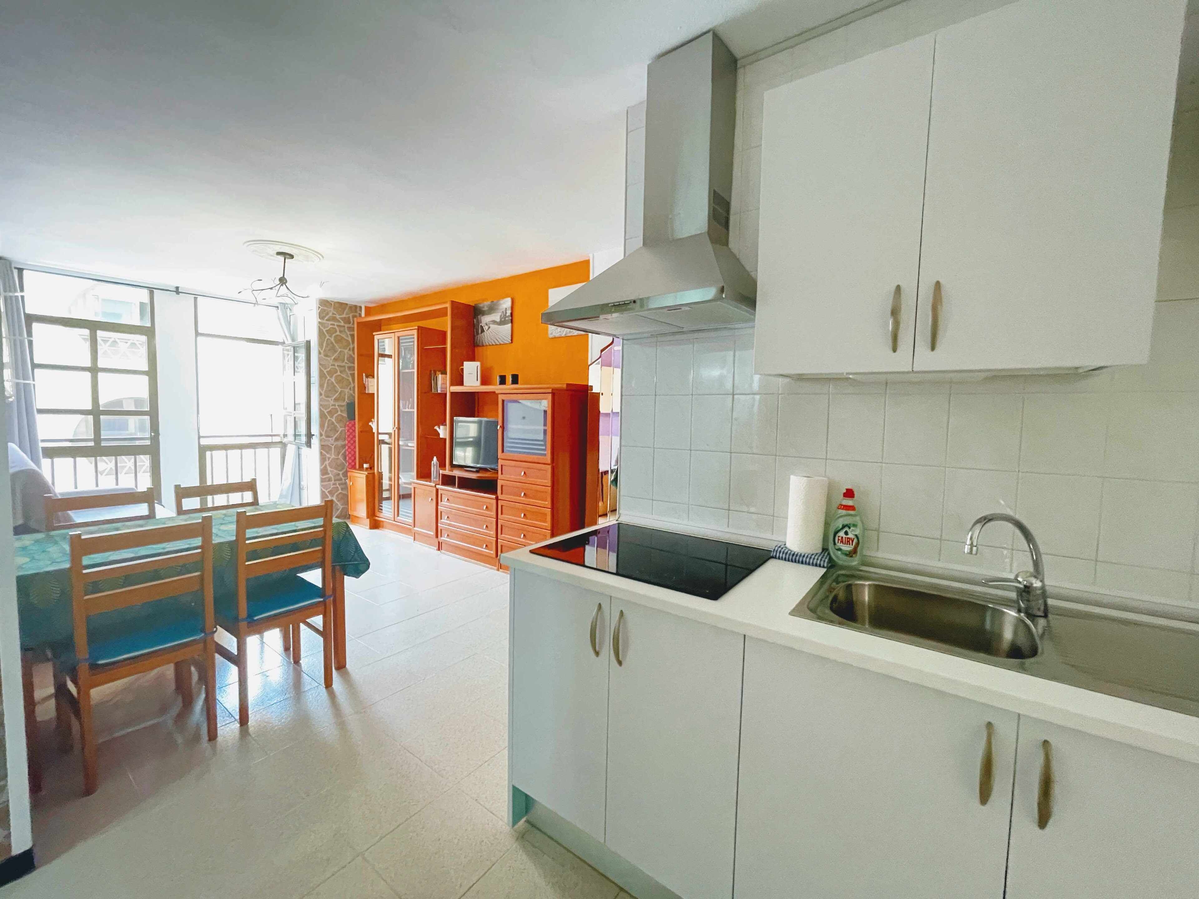 A kitchen with white cabinets, a stainless steel sink, and a dining area with wooden chairs and a table.