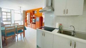 A kitchen with white cabinets, a stainless steel sink, and a dining area with wooden chairs and a table. - Semicorchea Corralejo Center iRent Fuerteventura (Corralejo)