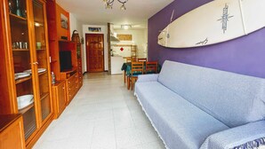 A compact living space with a sofa, wooden cabinets, a dining area, and a surfboard on the wall. - Semicorchea Corralejo Center iRent Fuerteventura (Corralejo)