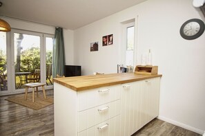 A modern kitchen with a wooden countertop, white cabinetry, and a sliding glass door leading to an outdoor seating area. - Cozy vacation apartment near the harbor - FeWos am Hochzeitsberg FeWo 08 - FeWos (Breege)