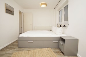 Une chambre à coucher avec un lit, des tables de chevet, un radiateur, une fenêtre et une porte.