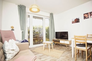 Ein modernes Wohnzimmer mit einer Couch, einem Fernseher, Holzmöbeln und Blick durch Glastüren auf einen Außenbereich.