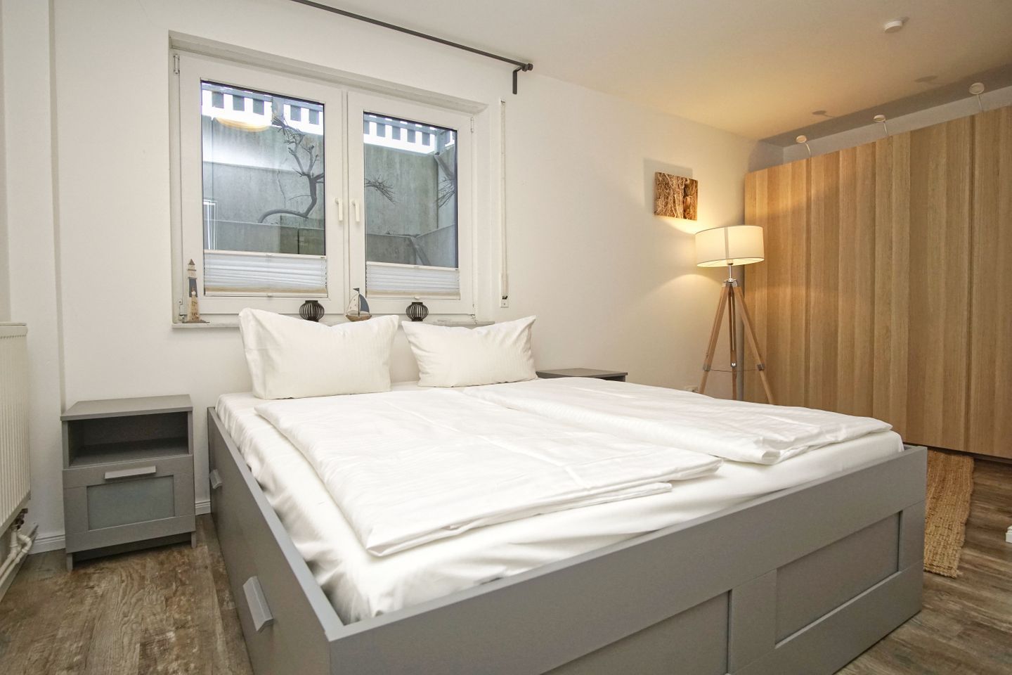 Ein Schlafzimmer mit einem Bett, zwei Nachttischen, einer Lampe, einem Fenster mit Jalousien und einem Holzschrank.