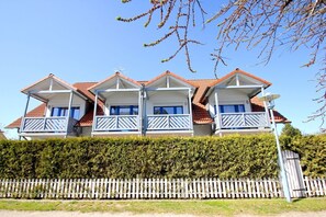 A three-story house with a red-tiled roof, multiple balconies, and a white picket fence. - Cozy vacation apartment near the harbor - FeWos am Hochzeitsberg FeWo 08 - FeWos (Breege)