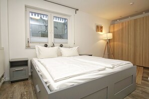 A bedroom with a bed, two bedside tables, a lamp, a window with blinds, and a wooden wardrobe. - Cozy vacation apartment near the harbor - FeWos am Hochzeitsberg FeWo 08 - FeWos (Breege)