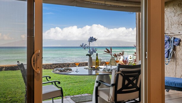 A dining area with a view of the ocean, a table set with a bottle, glasses, and decorative items.