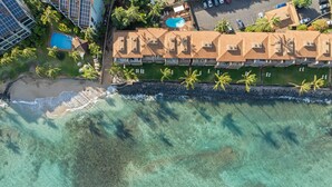 An aerial view of a coastal hotel with a swimming pool, palm trees, and a beach.