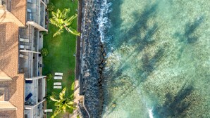 An aerial view of a beachfront hotel with multiple balconies, a pool area, and a rocky shoreline.