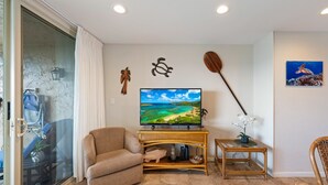 A living room with a television, a sofa, a small table with a plant, and a wall-mounted paddleboard.