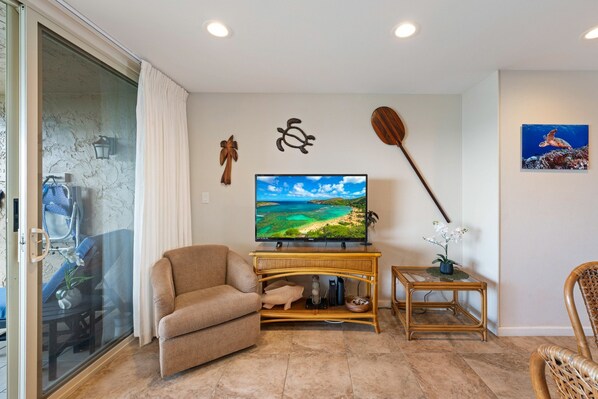 A living room with a television, a sofa, a small table with a plant, and a wall-mounted paddleboard.