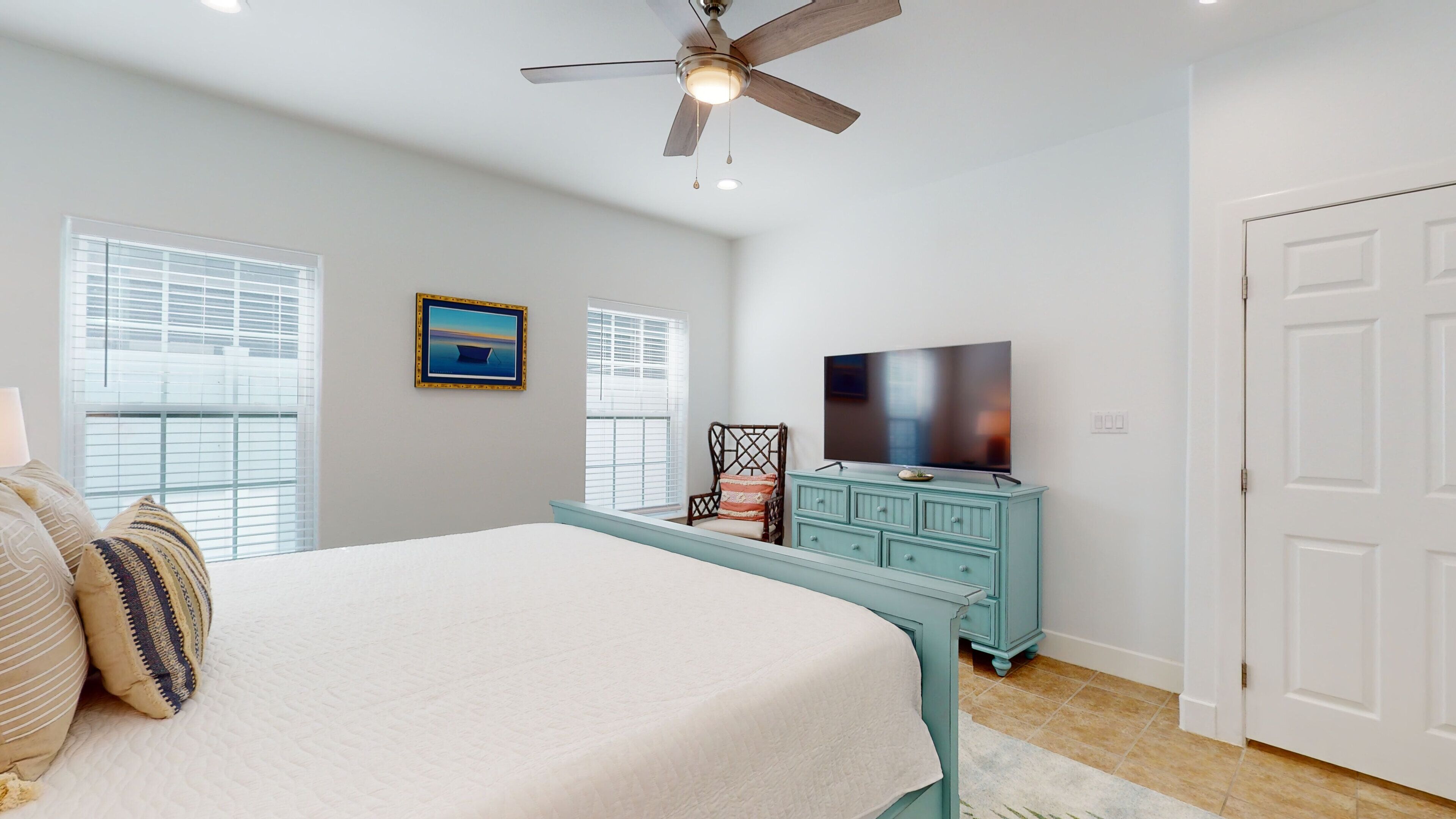 A bedroom with a bed, a ceiling fan, a TV, a dresser, and a door.