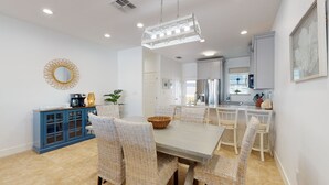 Un espace repas moderne avec une grande table, des chaises en osier et un buffet bleu.