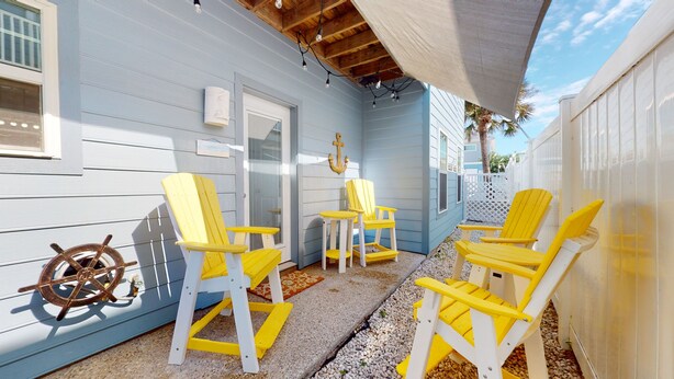 Un espace extérieur abrité, aménagé avec des chaises jaunes et décoré d’un gouvernail de bateau.