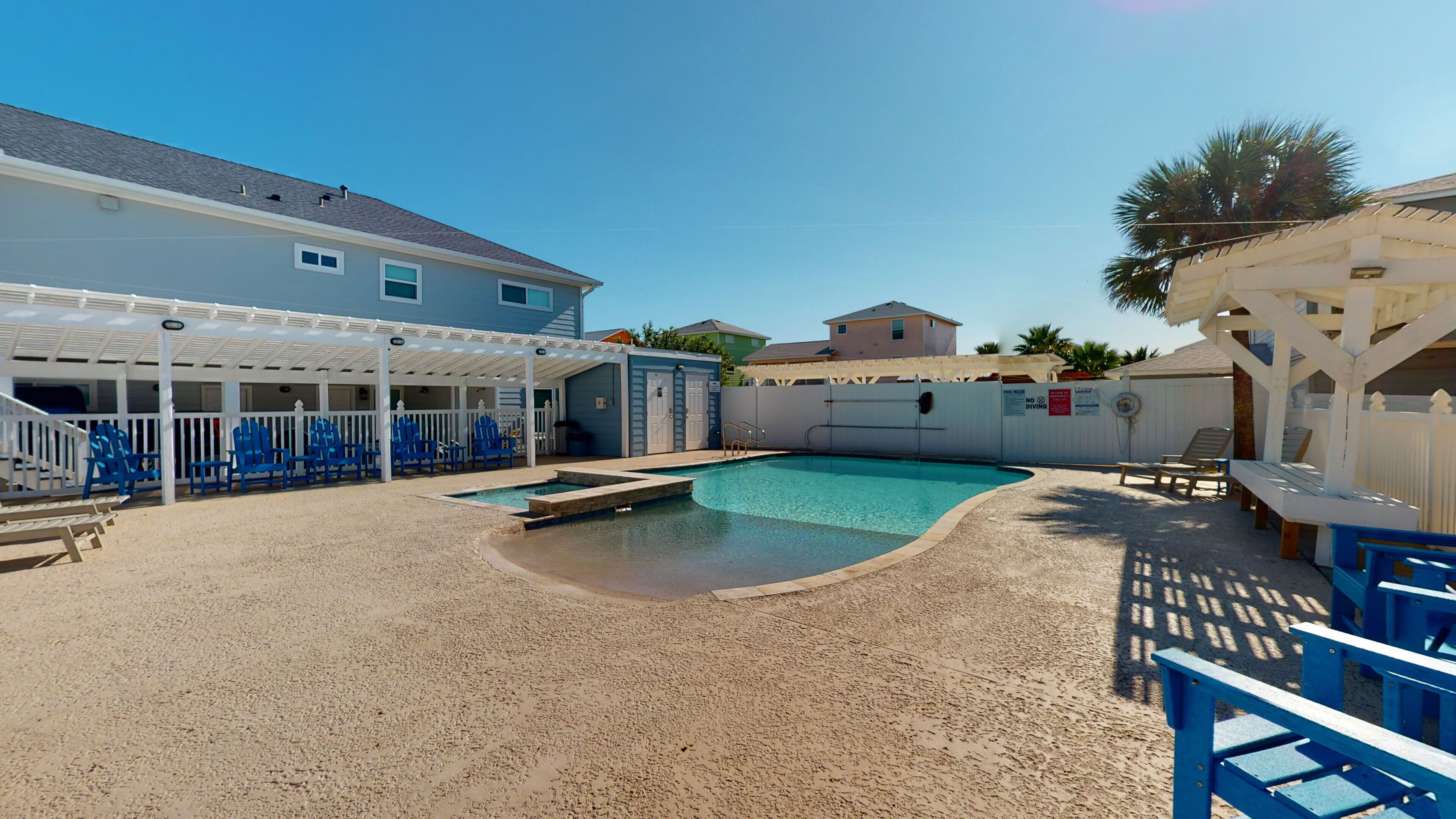 A backyard with a swimming pool, blue chairs, and a covered seating area.