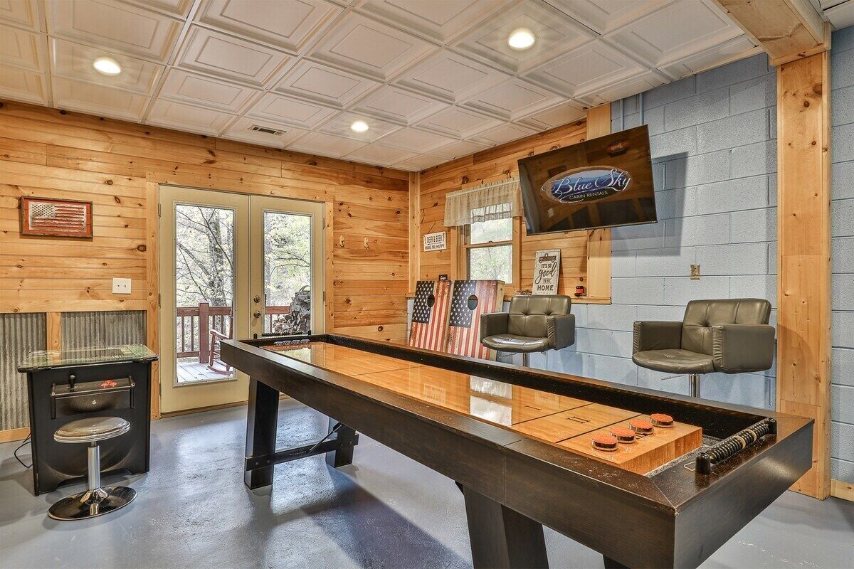Une table de billard dans une pièce aux murs en bois, avec un téléviseur fixé au mur et deux fauteuils en cuir.