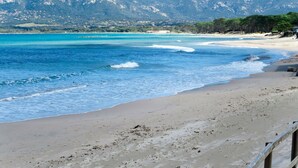 Une plage à l’eau d’un bleu cristallin, bordée d’un rivage sablonneux, avec une chaîne de montagnes en toile de fond.