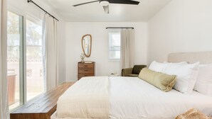 Une chambre à coucher avec un grand lit, un ventilateur de plafond, un banc en bois, une commode et une fenêtre avec des rideaux.