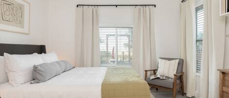 Un dormitorio con cama, una silla, ventilador de techo y ventana con cortinas.