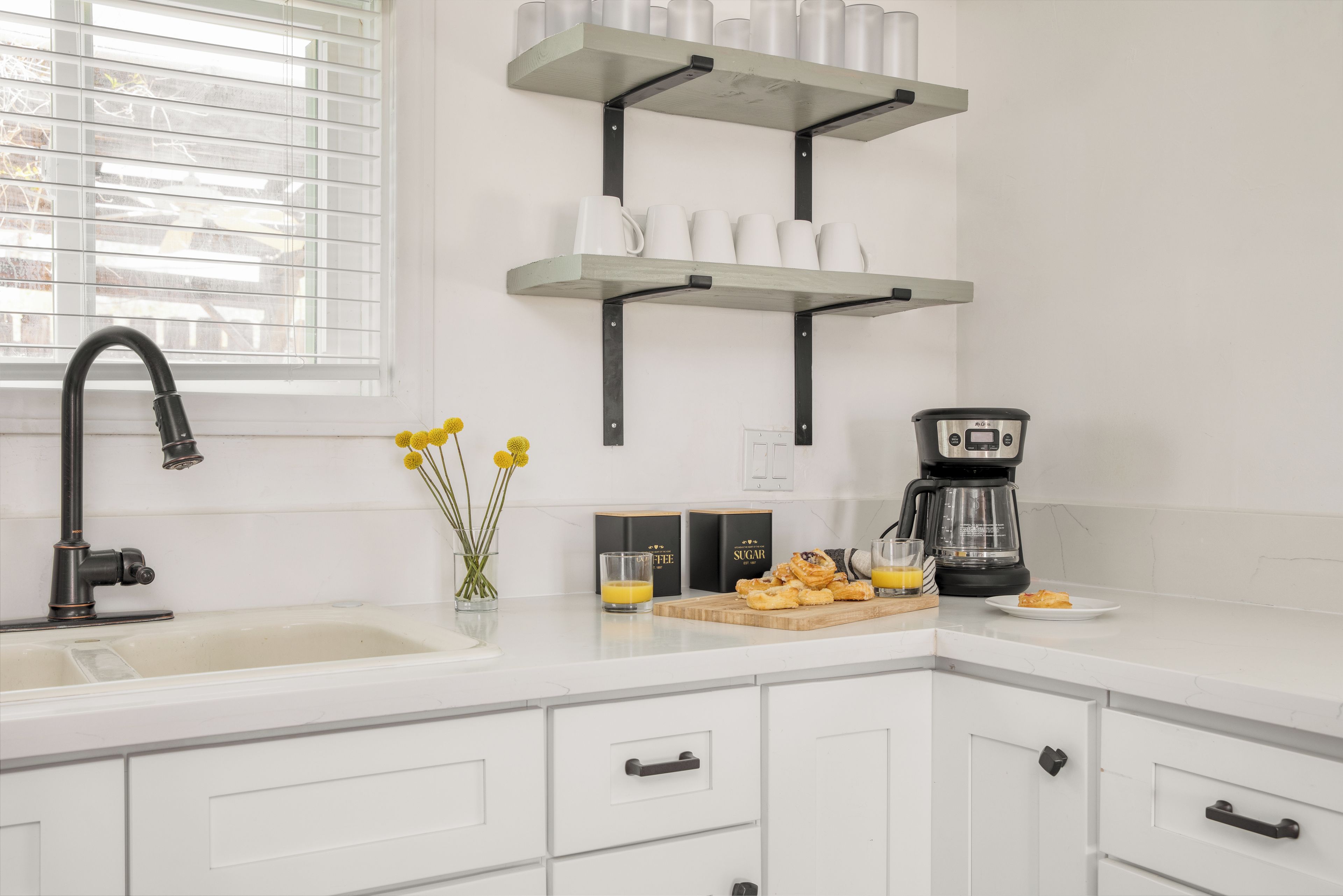 A kitchen with white cabinets, a black faucet, a coffee maker, and a cutting board with food.