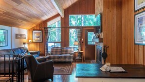 A cozy cabin interior with wooden walls, a sofa, a dining table, and a fireplace.