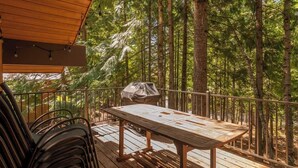 A deck with a table and chairs, surrounded by a forest.