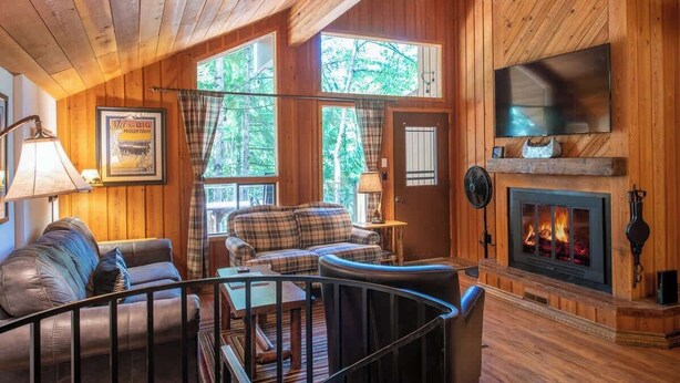 A cozy cabin interior with a fireplace, wooden walls, and a plaid sofa.
