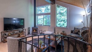 Ein gemütliches Wohnzimmer mit Kamin, großen Fenstern, einem Fernseher und einer Treppe.
