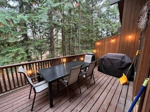 A wooden deck with a table and chairs, surrounded by trees. - Escape to Ptarmigan Village 90 (Whitefish)