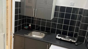 Una cocina compacta con un lavamanos de acero inoxidable, lavadora integrada y paredes de azulejos negros.