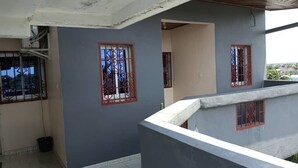 Un immeuble résidentiel à l’extérieur gris, doté de deux fenêtres aux encadrements rouges et d’un balcon bien visible.
