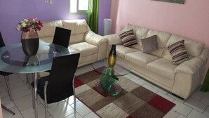 Un salon comprenant une table à manger en verre, deux canapés, une table basse en verre vert et un tableau représentant un phare accroché au mur.