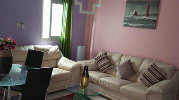 Un soggiorno con un divano beige, un tavolino in vetro e un quadro raffigurante un faro appeso al muro.