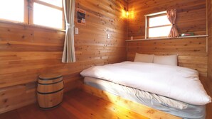 A wooden cabin room with a bed, a window, a curtain, and a wooden barrel. - Glamping Village LEAF (Mashiki)