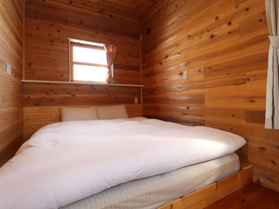 Een houten kamer met een bed, een raam met gordijnen en een houten wand.