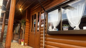 A wooden cabin with a stone-tiled porch, a large window with lace curtains, and a potted plant on the windowsill. - Glamping Village LEAF (Mashiki)