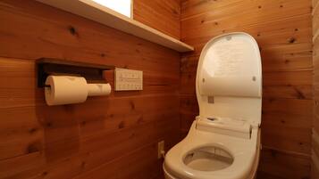 A wooden-paneled bathroom with a toilet, a paper towel dispenser, and a window above the toilet.