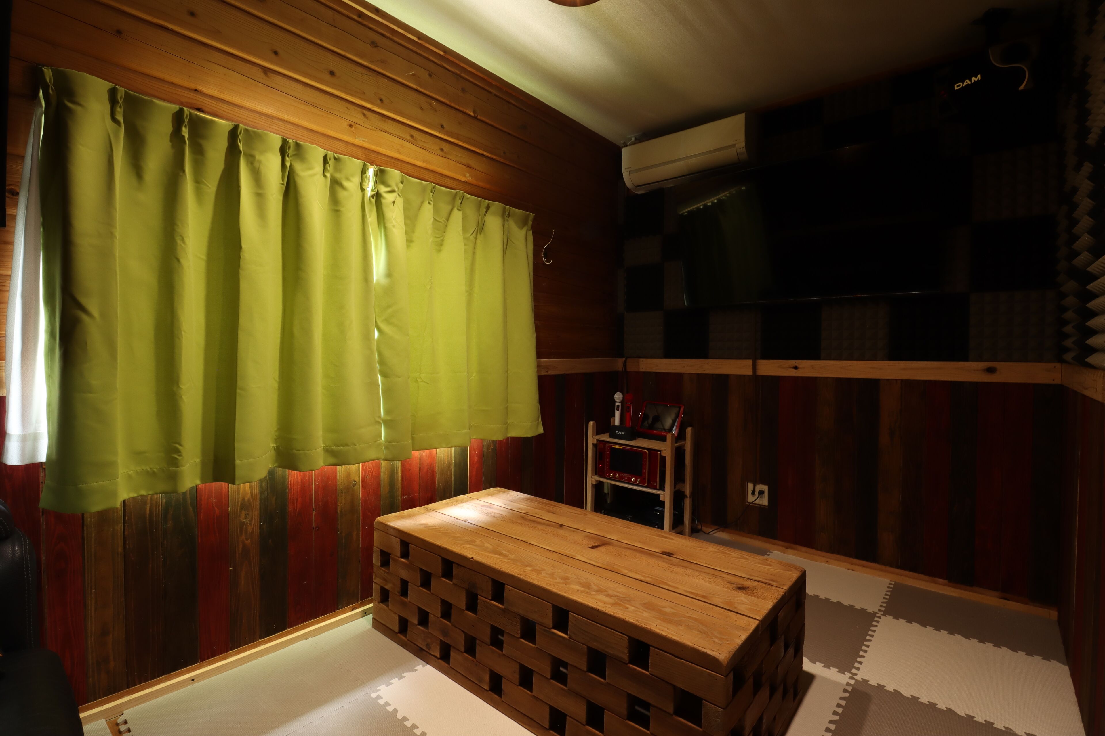 Een kamer met houten paneelwanden, een groen gordijn, een houten bankje en een klein plankje met een magnetron.