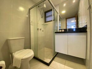 Et moderne badeværelse med en glasafskærmet brusekabine, et toilet og et hvidt skab.