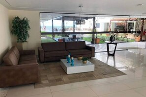 En moderne stue med en brun sofa, et hvidt sofabord og en stor glasdør, der fører ud til et udendørs område.