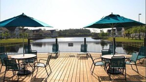 Eine Holzterrasse mit Sitzgelegenheiten und Sonnenschirmen mit Blick auf ein Gewässer.