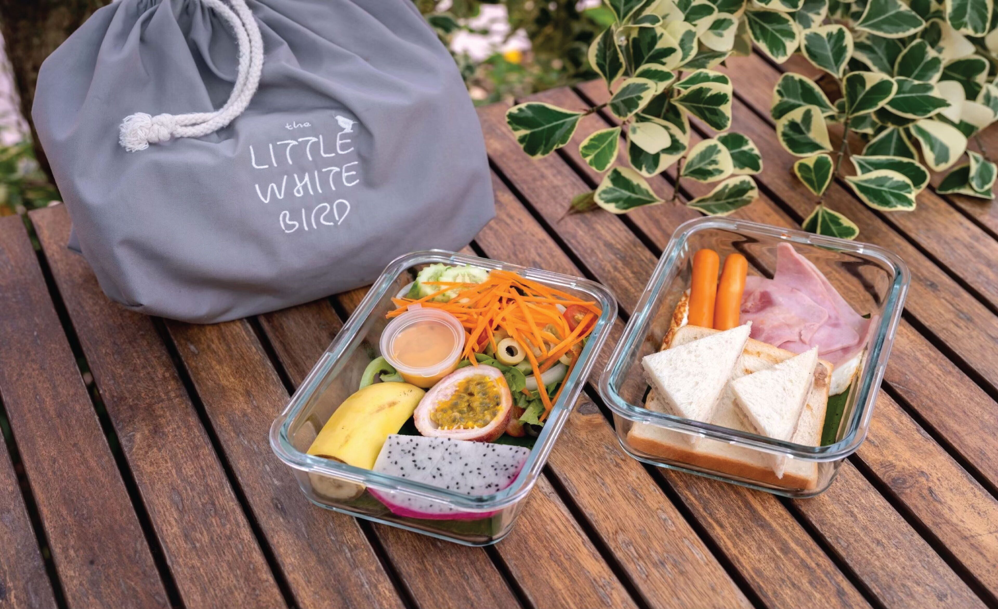 Dos recipientes de vidrio con alimentos sobre una mesa de madera, junto a una bolsa gris de cordón con texto.